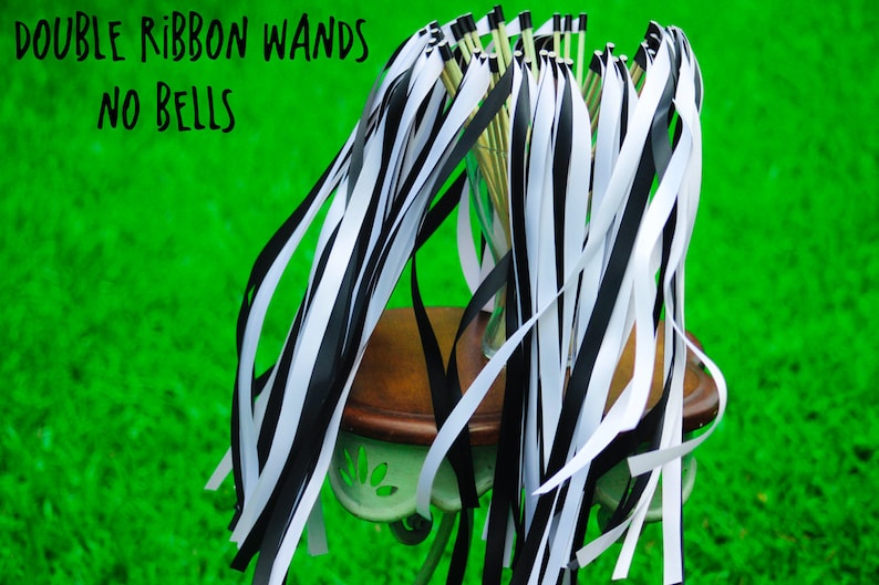 May include: A bunch of black and white ribbon wands with no bells. The wands are tied together and sitting on a small table. The table is on a green grassy surface.
