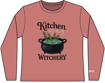 Może przedstawiać: Koszulka z długim rękawem w kolorze przydymionego różu z czarną grafiką kotła i napisem "Kitchen Witchery". Kociołek zawiera zielone zioła i wydziela parę. Słowo "queen" jest nadrukowane na prawym rękawie.