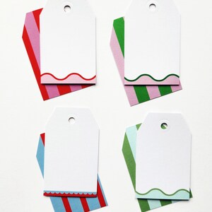 May include: Four white gift tags with a curved edge design, each resting on a colorful striped background. The backgrounds are red and pink, green and pink, red and blue, and green and blue. Each tag has a hole at the top.