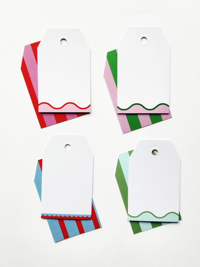 May include: Four white gift tags with a curved edge design, each resting on a colorful striped background. The backgrounds are red and pink, green and pink, red and blue, and green and blue. Each tag has a hole at the top.