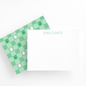 May include: A white card with a green checkered pattern featuring white bunnies and green leaves. The card has the name "Sophia Elizabeth" printed in black at the top.