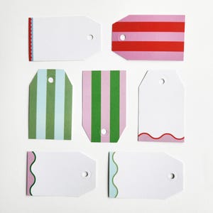 May include: A collection of blank gift tags in various designs. Some tags feature stripes in pink, red, and green. Others have decorative edges in red, pink, and green. Each tag has a hole for attaching to a gift.