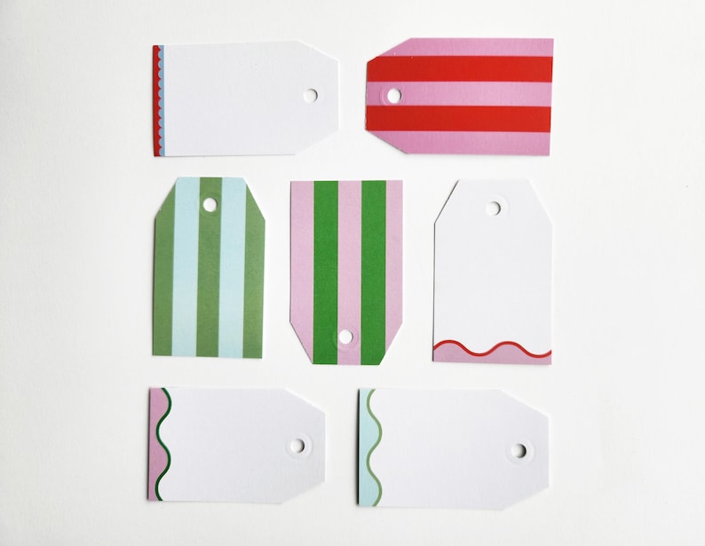 May include: A collection of blank gift tags in various designs. Some tags feature stripes in pink, red, and green. Others have decorative edges in red, pink, and green. Each tag has a hole for attaching to a gift.
