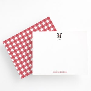 Puede incluir: Una tarjeta blanca con una ilustración de una vaca en blanco y negro y el texto "JACK CHESTER" impreso en negro. La tarjeta está parcialmente cubierta por un patrón de cuadros rojos y blancos.
