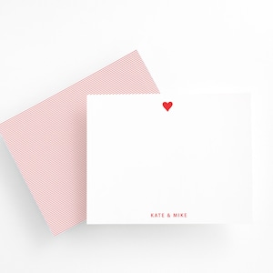 Peut inclure: Un ensemble de papeterie blanc avec un cœur rouge et les noms "KATE & MIKE" imprimés en rouge. L'ensemble comprend une carte blanche et une enveloppe à rayures rouges et blanches. La papeterie est sur fond blanc.