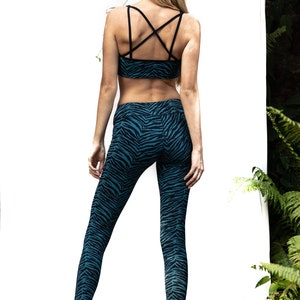 May include: A woman wearing a black and teal zebra print sports bra and leggings. The bra has a criss-cross back strap design.
