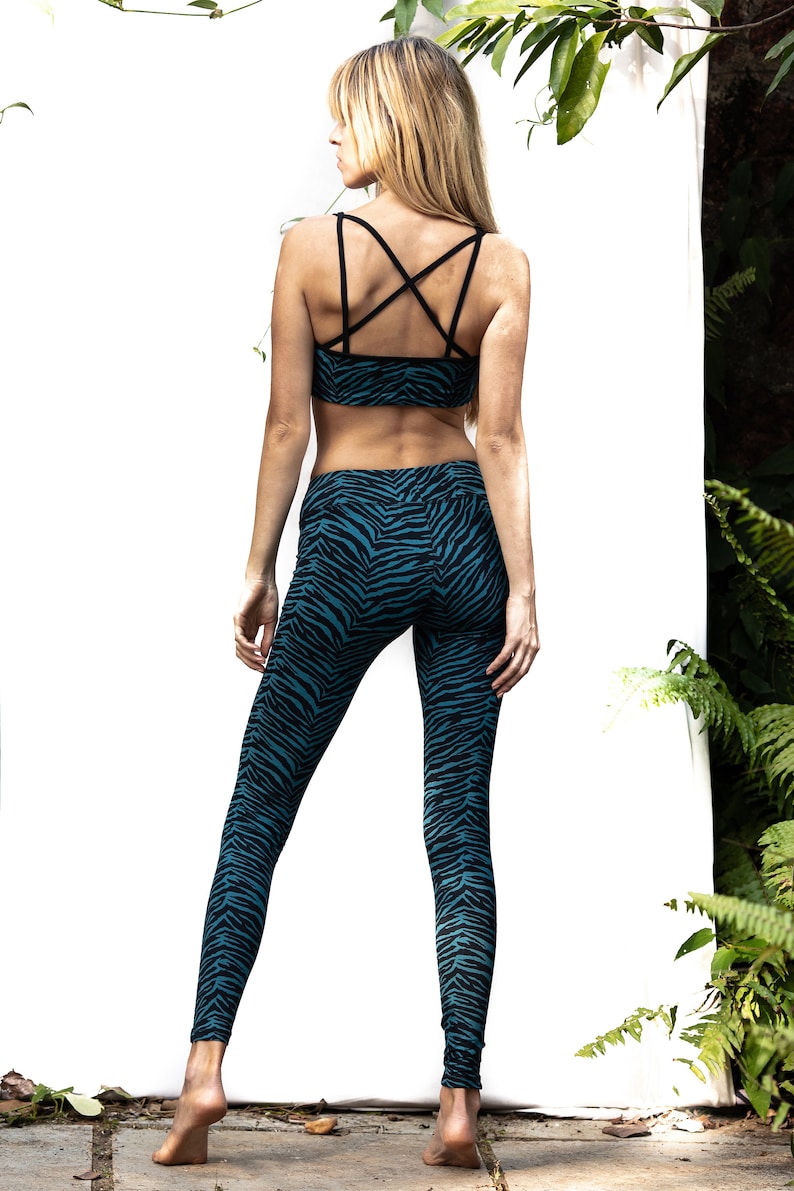 May include: A woman wearing a black and teal zebra print sports bra and leggings. The bra has a criss-cross back strap design.