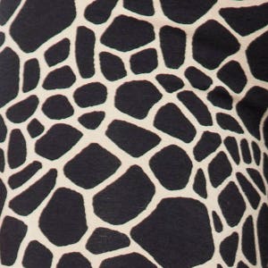 May include: Close-up of a fabric with a giraffe print pattern. The design features irregular dark brown shapes outlined with a cream color, creating a repeating pattern. The fabric appears to be soft and textured.