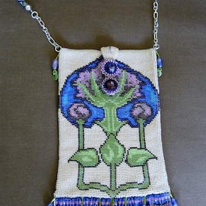 Puede incluir: Un bolso blanco de cuentas con un diseño floral en tonos azules, verdes y morados. El bolso tiene una franja de cuentas y una correa de cadena plateada.