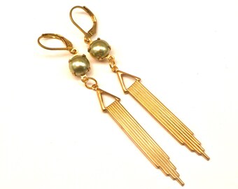 May include: Gold dangle earrings with a green pearl accent and a geometric design. The earrings have a lever back closure.