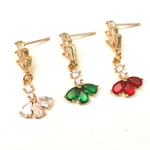 May include: Three pairs of gold dangle earrings with clear and colored stones. The earrings have a geometric design with a teardrop shape at the bottom. The teardrop shapes are clear, green, and red.