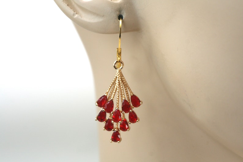 Puede incluir: Pendientes colgantes dorados con un dise&ntilde;o en forma de abanico adornados con numerosas piedras preciosas rojas en forma de l&aacute;grima. Los pendientes cuelgan de un gancho dorado, presentando un estilo cl&aacute;sico y elegante. Las piedras preciosas son de color rojo intenso.