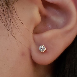 May include: A close-up of a person's ear with a small, round, clear diamond stud earring.