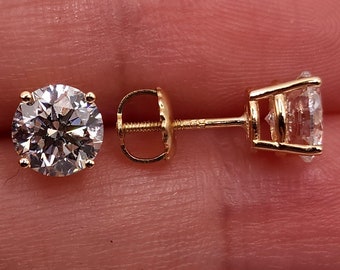 May include: A pair of gold stud earrings with round, clear gemstones. The earrings are set in a classic four-prong setting, showcasing the brilliance of the stones. The posts and backs are also gold, creating a cohesive and elegant look.