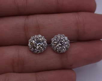 Può includere: Due orecchini a lobo rotondi color argento con un gruppo di piccole pietre trasparenti. Gli orecchini sono presentati su uno sfondo chiaro. Ogni orecchino ha un diametro di circa 1 cm.