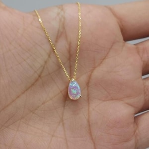 Könnte beinhalten: Eine zarte goldene Kettenkette mit einem tropfenförmigen Opal-Anhänger. Der Opal ist schillernd in Rosa-, Weiß- und Blautönen.