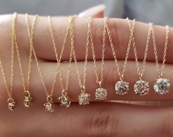 May include: A set of nine gold necklaces with small diamond pendants. The necklaces are arranged in a row on a hand, with the pendants increasing in size from left to right.