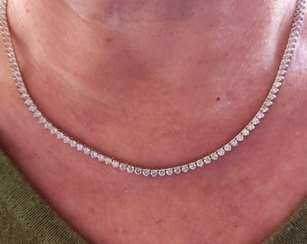 May include: A silver necklace with a row of small, clear diamonds.