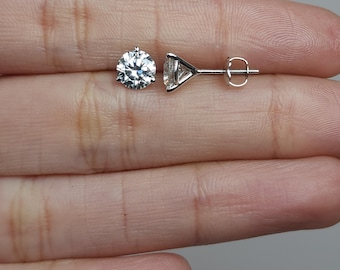 May include: Two silver stud earrings with round, clear gemstones. One earring is fully assembled, showing the post and backing. The other earring is a close-up of the gemstone. The earrings are displayed on a neutral background.