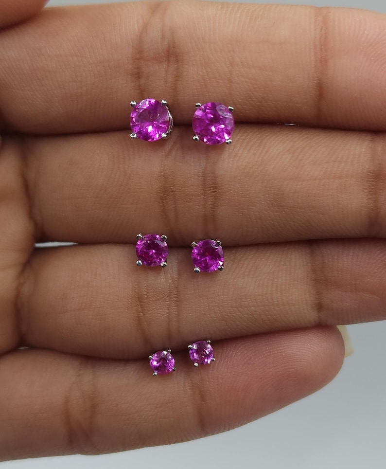 May include: Three pairs of pink gemstone earrings with silver settings. The earrings are arranged in order of size, with the largest pair at the top and the smallest pair at the bottom.
