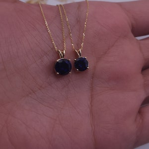 May include: Two gold necklaces with blue gemstone pendants. The necklaces are on a hand.