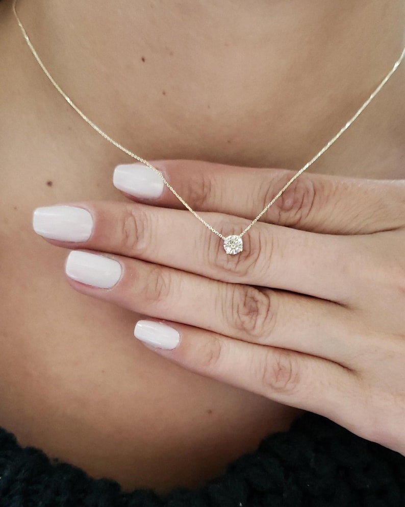 Puede incluir: Un delicado collar de cadena de oro con un peque&ntilde;o colgante redondo de diamante transparente.