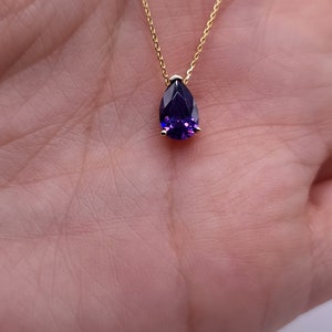 May include: A gold chain necklace with a pear-shaped purple gemstone pendant.