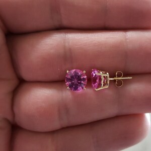 May include: A pair of gold earrings with pink round gemstones. The earrings are 8mm in size.