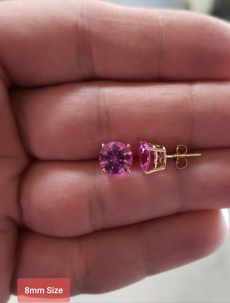 May include: A pair of gold earrings with pink round gemstones. The earrings are 8mm in size.