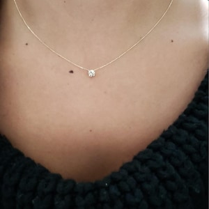 Puede incluir: Un delicado collar de cadena de oro con un solo colgante de piedra preciosa redonda y transparente.
