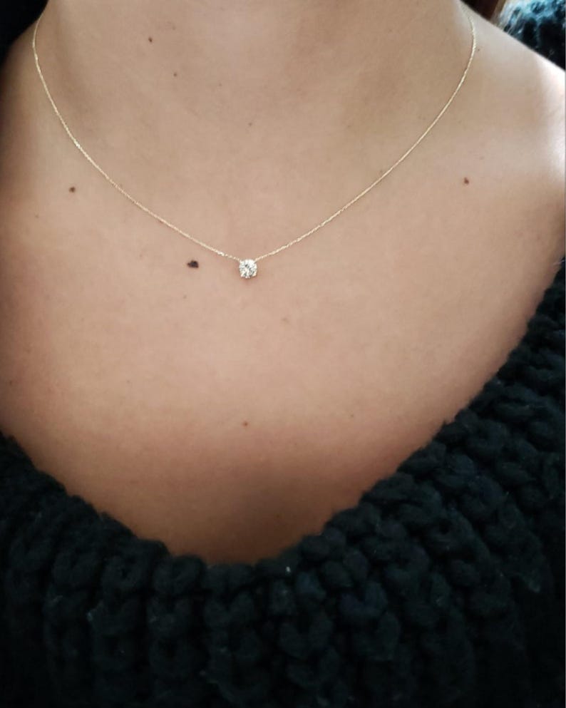 Puede incluir: Un delicado collar de cadena de oro con un solo colgante de piedra preciosa redonda y transparente.