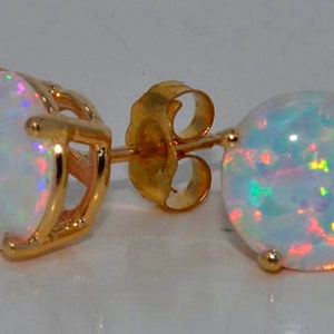 Puede incluir: Un par de pendientes de botón de oro con piedras redondas de ópalo blanco. Los ópalos tienen un brillo iridiscente arcoíris.