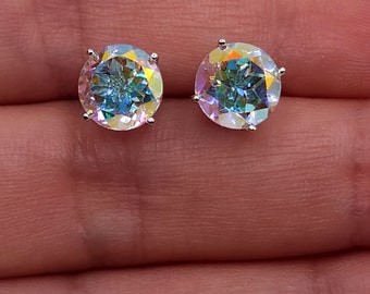 May include: A pair of round, iridescent stud earrings. Each earring features a large, faceted gemstone with a rainbow of colors, set in a silver-toned metal. The earrings are displayed against a neutral background.
