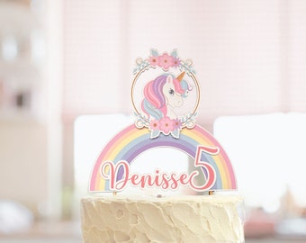 May include: A white cake with a rainbow and unicorn topper. The topper says "Dennisse 5".