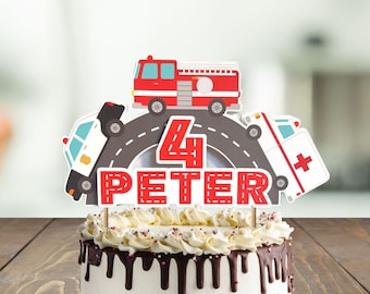 May include: A red, white, and blue cake topper with a fire truck, police car, and ambulance driving on a road. The topper says "4 Peter" on it. The cake topper is on top of a chocolate cake with white frosting and red sprinkles.