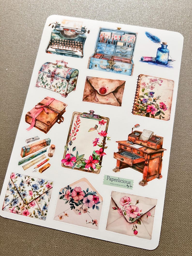 May include: A sheet of vintage-style stickers featuring images of a typewriter, a vintage suitcase, a floral-patterned box, envelopes, a book, a clipboard, a desk with a typewriter, and an inkwell with a quill pen. The stickers are printed on white paper and have a watercolor-like appearance. The text "Paperlicious by Sue" is printed in the bottom right corner.