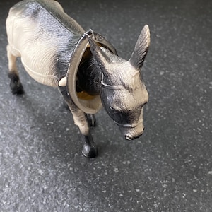 Könnte beinhalten: Kleine Eselfigur aus Kunststoff in Grau- und Schwarztönen. Der Esel hat ein Geschirr und steht auf einer dunklen Oberfläche. Die Figur ist ein Spielzeug oder ein Sammlerstück.