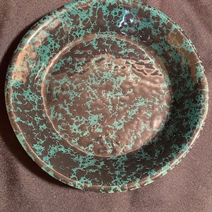 May include: A round plate with a speckled pattern in black and teal. The plate has a slightly raised rim and a smooth, glossy finish. The teal spots are distributed across the black surface.