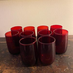 May include: Set of ten ruby red glass tumblers. The glasses are clear and have a slightly rounded shape.