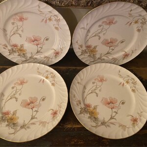May include: Set of four white porcelain dinner plates with a delicate floral design featuring pink poppies and green leaves. The plates have a gold rim and a subtle rippled texture.