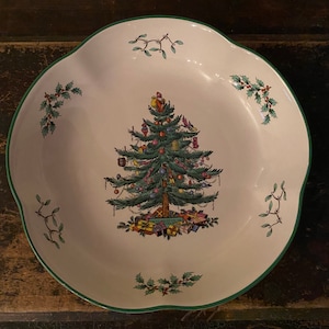 May include: A white, scalloped-edge serving dish with a green border. The center features a detailed illustration of a decorated Christmas tree with presents beneath it. Sprigs of holly and mistletoe are placed around the rim.