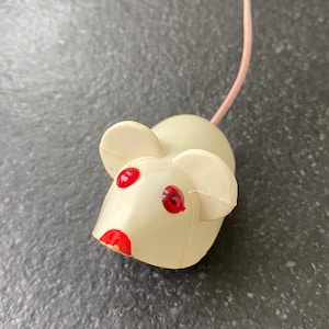 May include: A vintage toy mouse with a cream-colored body, large ears, and a pink tail. The mouse has red eyes and a red mouth. This toy is a classic children's plaything.