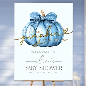 May include: A blue and gold welcome sign for a baby shower. The sign features a blue pumpkin with a gold bow and the text "A little pumpkin is on his way". The sign also says "Welcome to Alice's Baby Shower October 30th 2024".