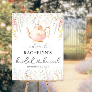 May include: A white welcome sign with a floral border and a pink teapot illustration. The text reads "Welcome to Rachelyn's Bridal Brunch September 10, 2024".