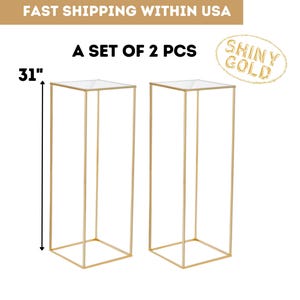 May include: Two gold metal display stands, each with a clear top and a rectangular frame. The stands are 31 inches tall. The text on the image says "A set of 2 pcs" and "Shiny Gold".