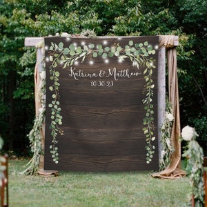 Può includere: Uno sfondo in legno rustico con vegetazione e luci a catena, perfetto per un matrimonio o un evento speciale. Lo sfondo presenta il testo "Katrina & Matthew 10-30-23".