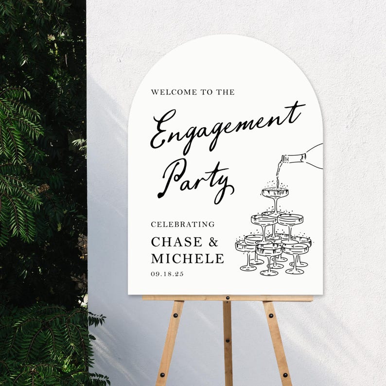 K&ouml;nnte beinhalten: Ein wei&szlig;es Schild mit schwarzem Text, das eine Verlobungsfeier f&uuml;r Chase & Michelle am 18. September 2025 ank&uuml;ndigt. Das Schild zeigt eine Grafik einer Champagnerpyramide mit einer Flasche, die Champagner in das oberste Glas gie&szlig;t.