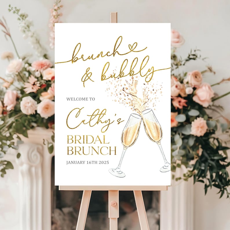 May include: A white sign on a wooden easel with gold text that reads "Brunch & Bubbly" and "Cathy's Bridal Brunch". Two champagne flutes are illustrated, with champagne pouring out. The date "January 16th 2025" is also displayed.