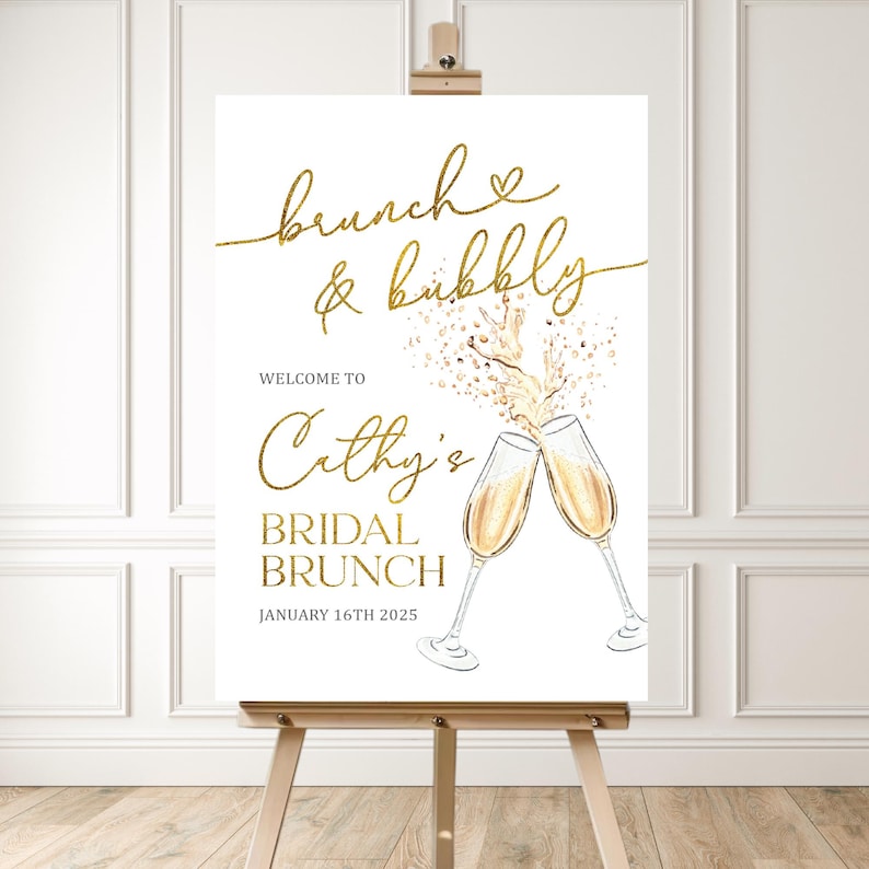 May include: A white sign on an easel with gold text that reads "brunch & bubbly" and "Cathy's Bridal Brunch". Two champagne flutes are illustrated, with champagne pouring out. The date "January 16th 2025" is also displayed.