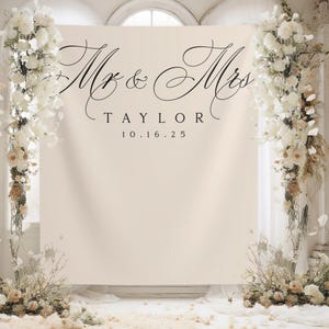 Könnte beinhalten: Ein weißer Hintergrund mit dem Text "Mr. & Mrs. TAYLOR 10.16.25" in schwarzer Kalligraphie. Der Hintergrund ist mit weißen Blumen auf beiden Seiten verziert.